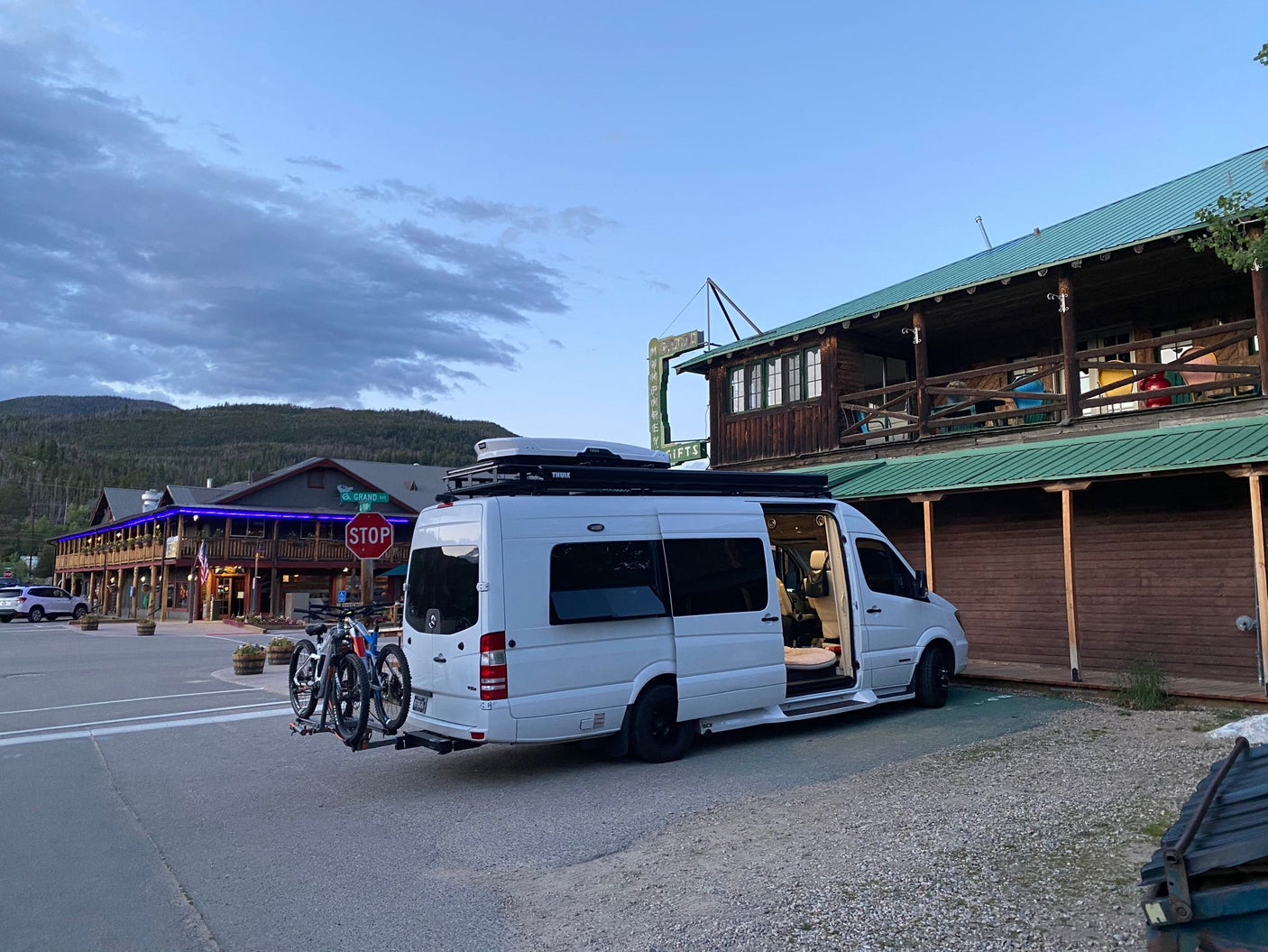 This RV rental Sprinter van with bikes is parked with its door open in a scenic mountain town.