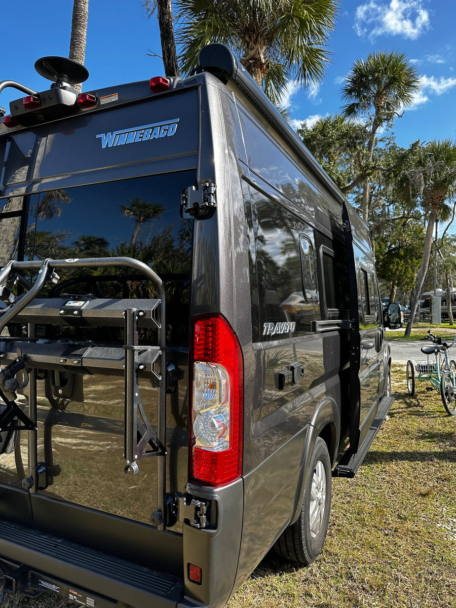 This dark Winnebago Travato RV rental is parked with a bike rack, ready for adventure under blue skies.