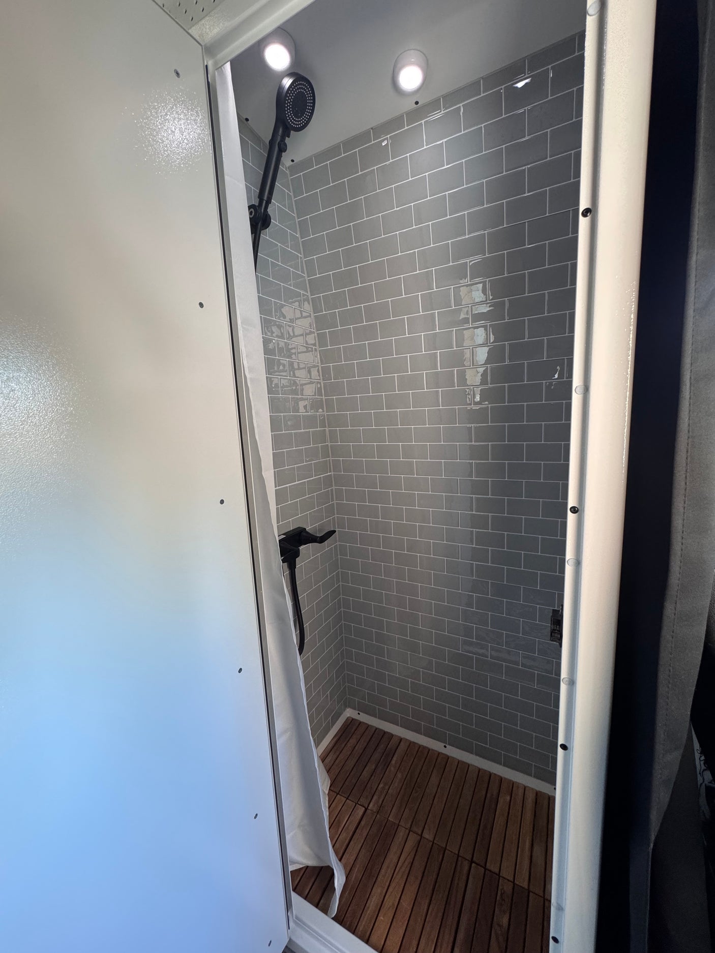RV rental's modern shower features gray subway tiles, a wooden slatted floor, and black fixtures.