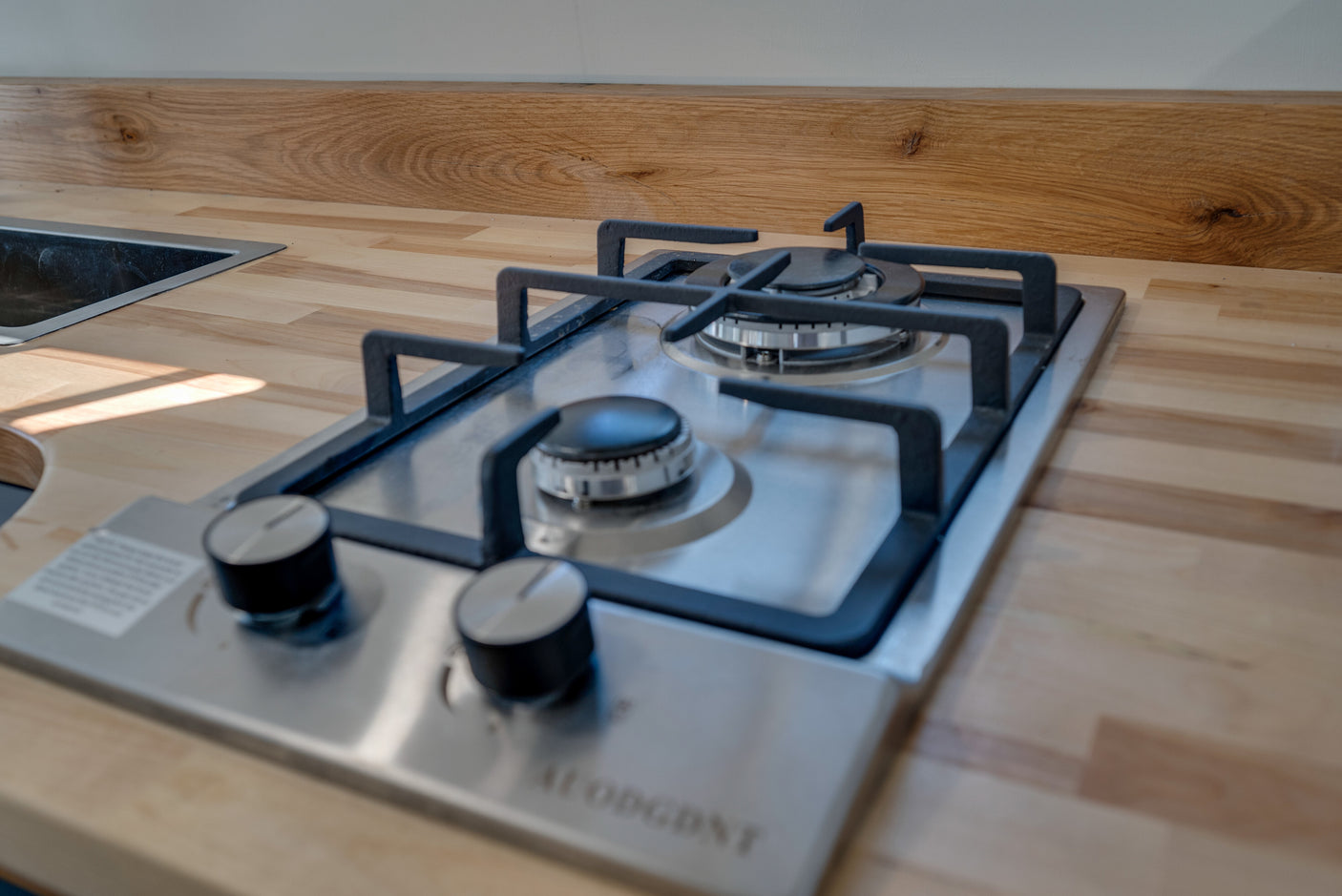 Compact RV rental kitchen with light wood countertop, stainless steel sink & 2-burner gas hob. Perfect for travel cooking.