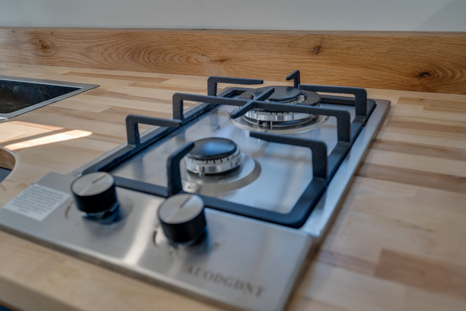 Compact RV rental kitchen with light wood countertop, stainless steel sink & 2-burner gas hob. Perfect for travel cooking.