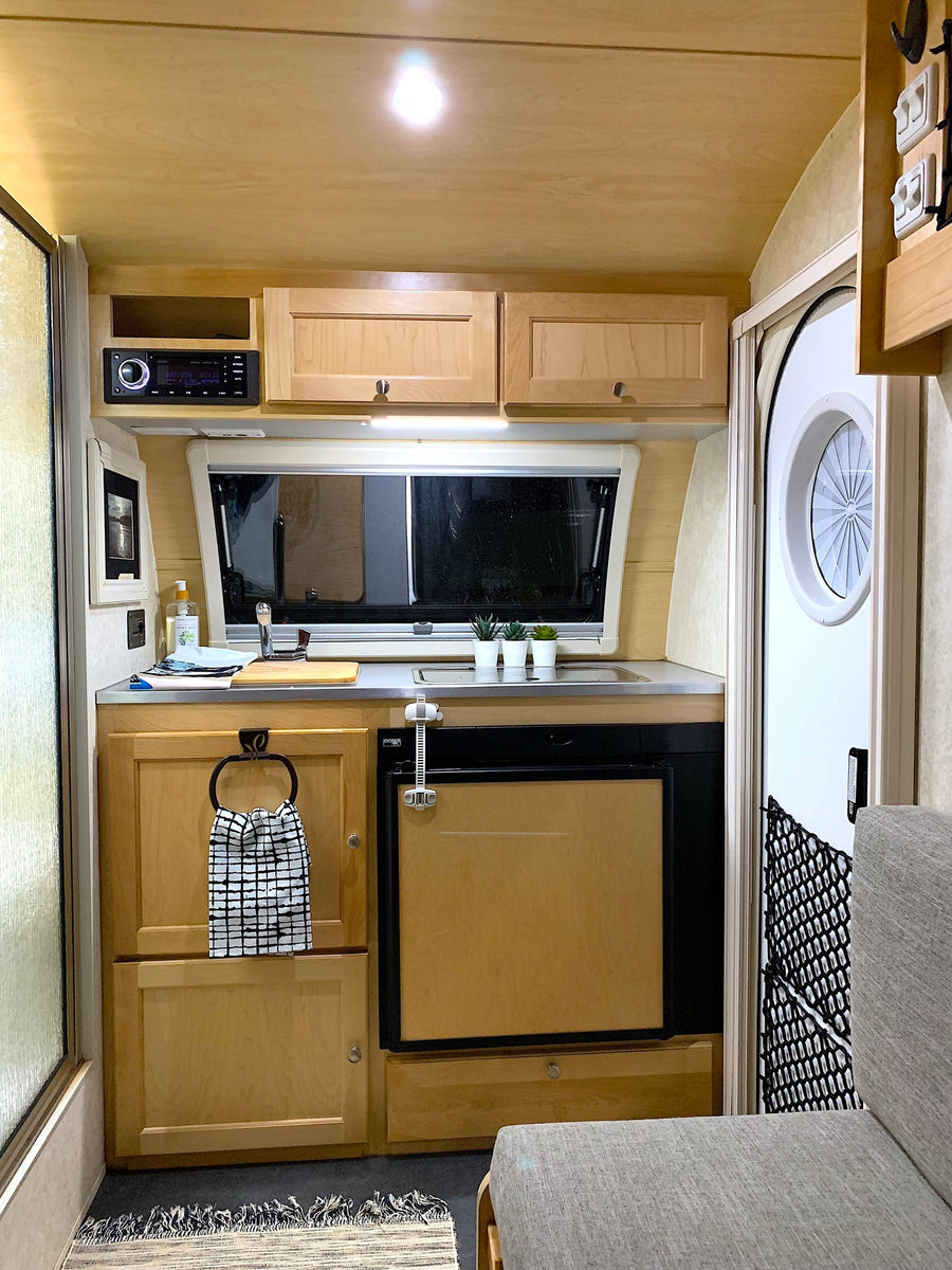 A compact RV rental kitchen with light wood cabinets, a sink, small fridge, and mounted stereo.