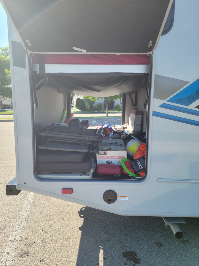 RV rental's spacious storage bay, well-packed with camping gear: chairs, a Weber grill, and sports equipment.