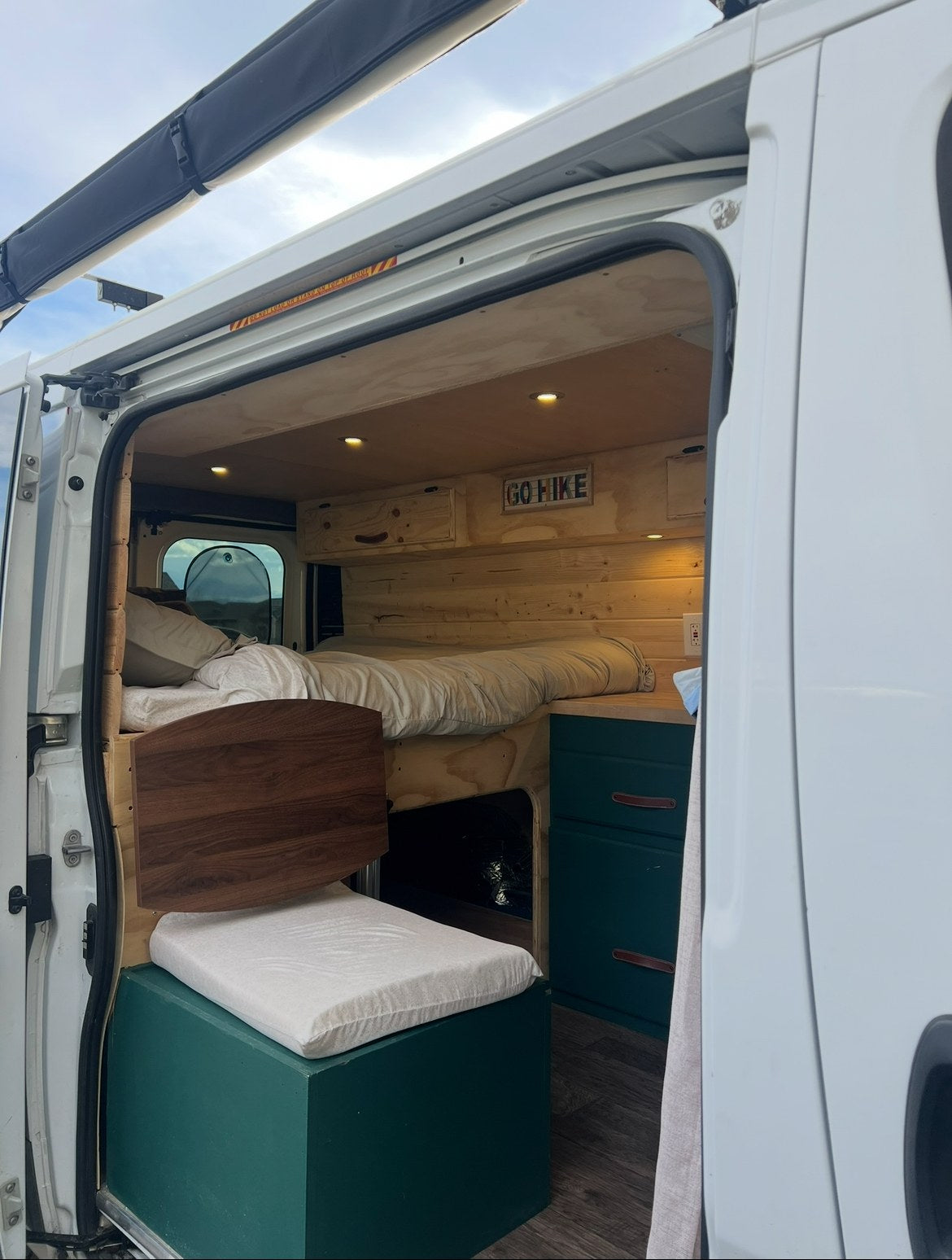 & open fields under a blue sky.|White Ram ProMaster van (likely an rv rental) parked by a vibrant elk mural on a modern building with wood siding.|This white RV rental van is parked next to a colorful mural depicting a moose