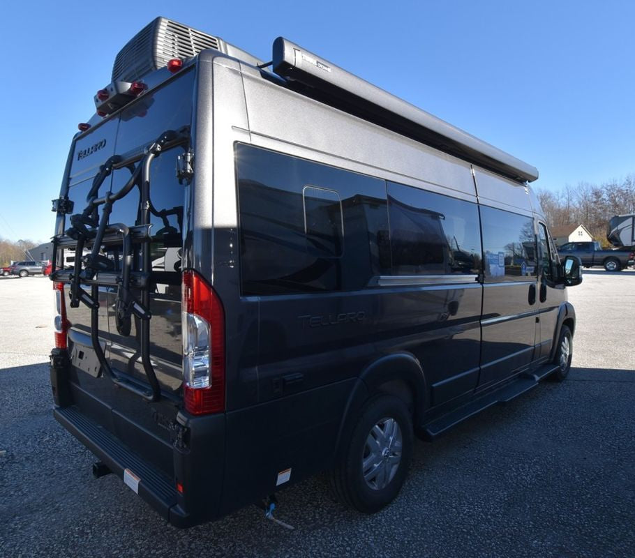 A dark gray Tellaro Class B camper van, equipped with a bike rack & awning, ready for RV rental.