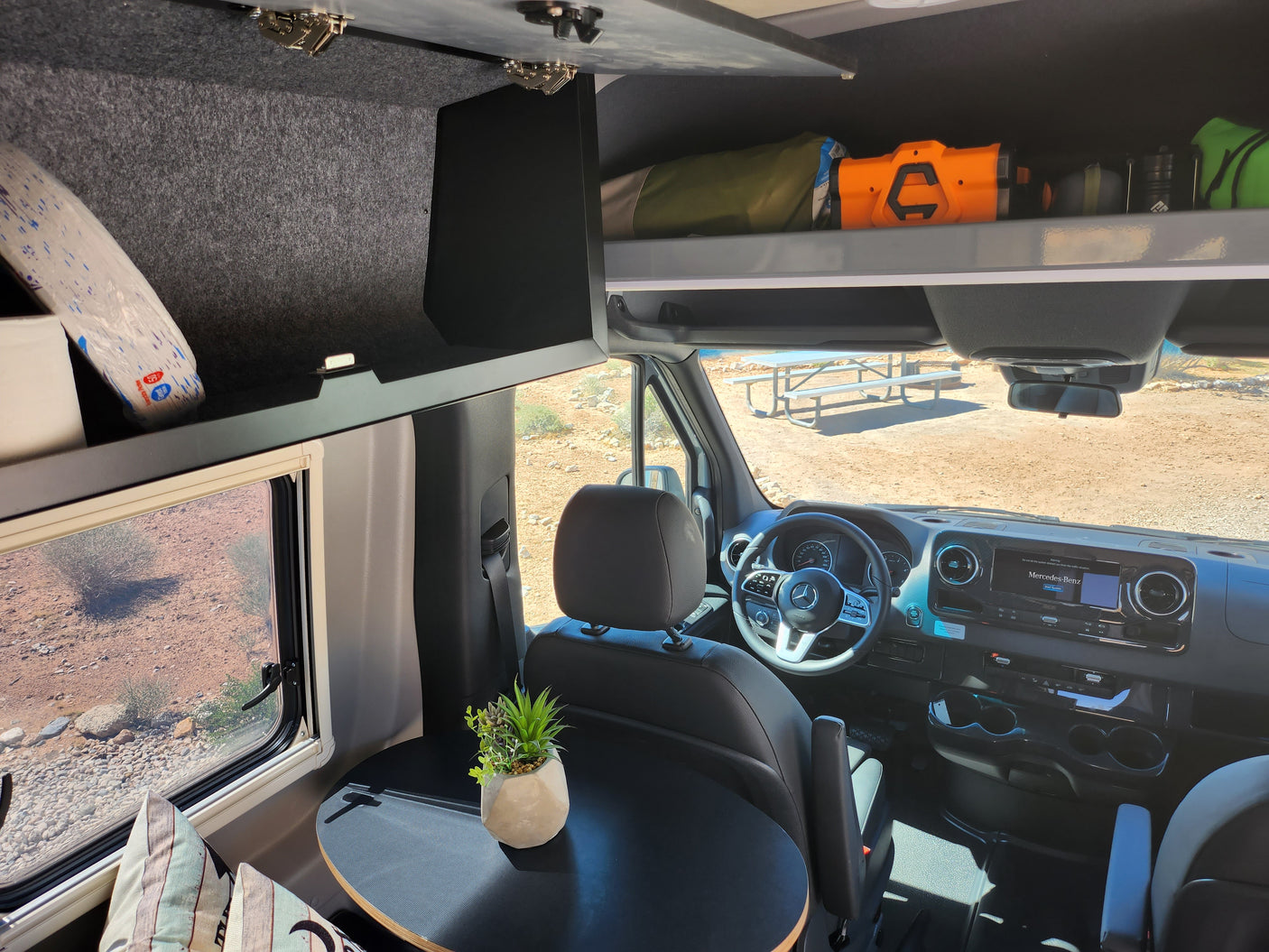 Spacious RV rental interior featuring the cockpit, overhead storage, and a cozy table, ready for desert adventures.