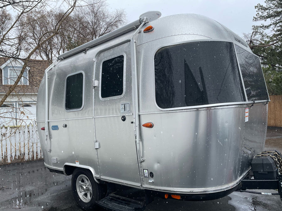 A shiny silver Airstream travel trailer, perfect for an rv rental, glistens with snowflakes while parked outdoors.