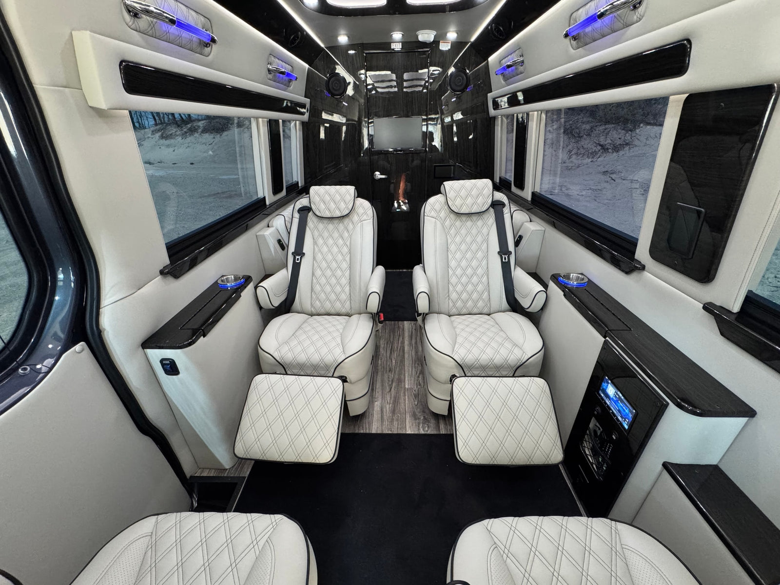 featuring an entertainment screen and control panel.|Luxurious RV rental interior with white quilted seats. Spacious customized van features premium finishes & scenic outdoor view.|Modern RV rental van interior showcasing the driver's cabin with white quilted seats and dashboard.|Premium RV rental interior: white quilted seats