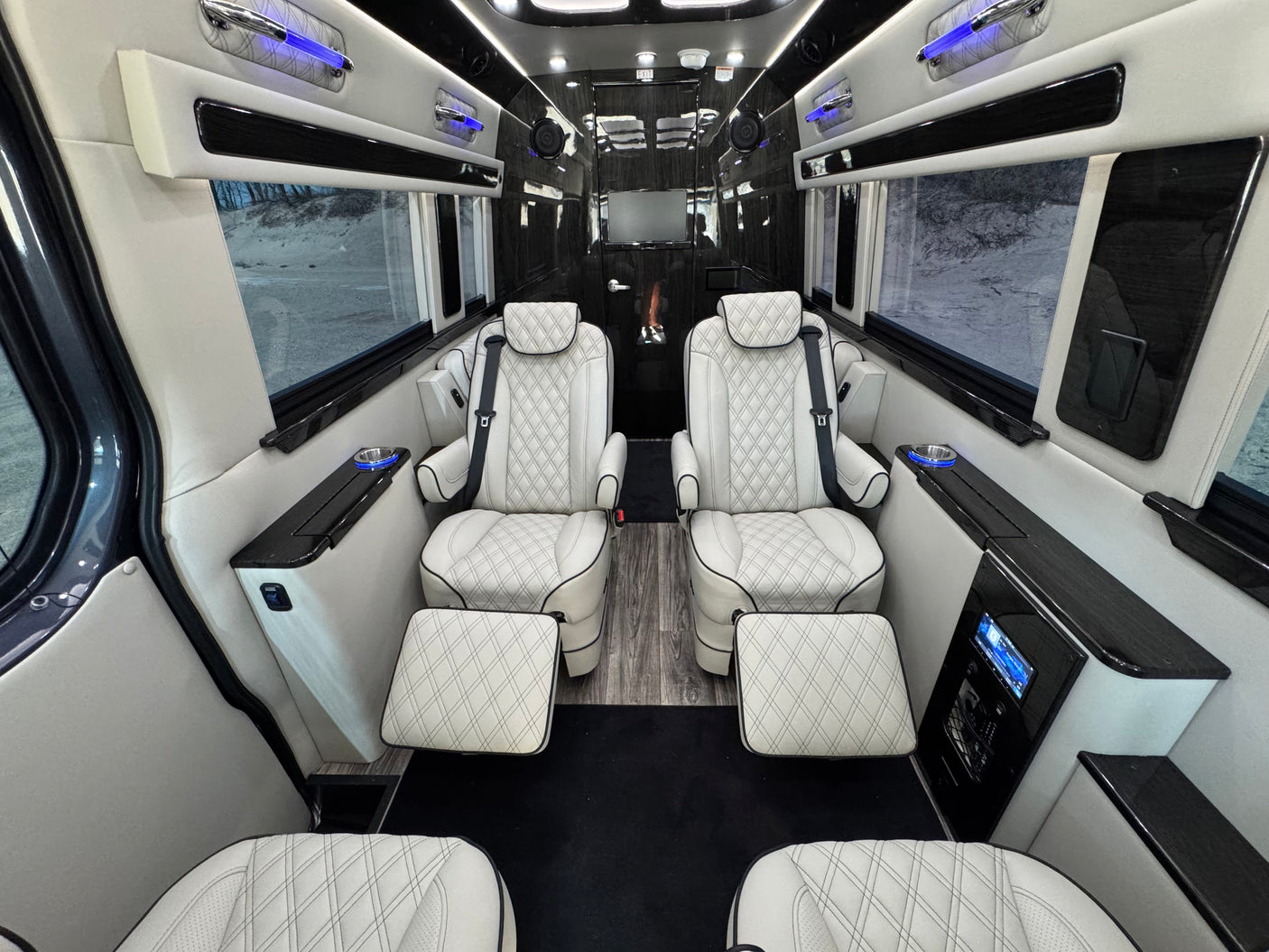 featuring an entertainment screen and control panel.|Luxurious RV rental interior with white quilted seats. Spacious customized van features premium finishes & scenic outdoor view.|Modern RV rental van interior showcasing the driver's cabin with white quilted seats and dashboard.|Premium RV rental interior: white quilted seats