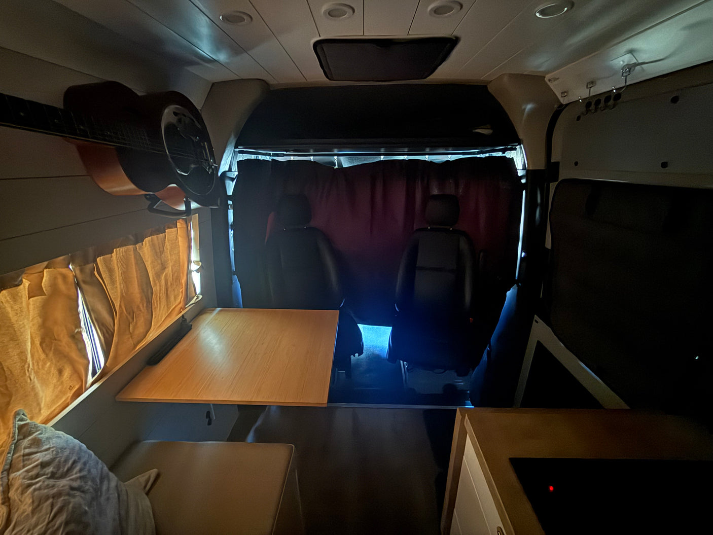 Inside this RV rental: a guitar, dining table, cozy seating, and front cabin privacy curtains.