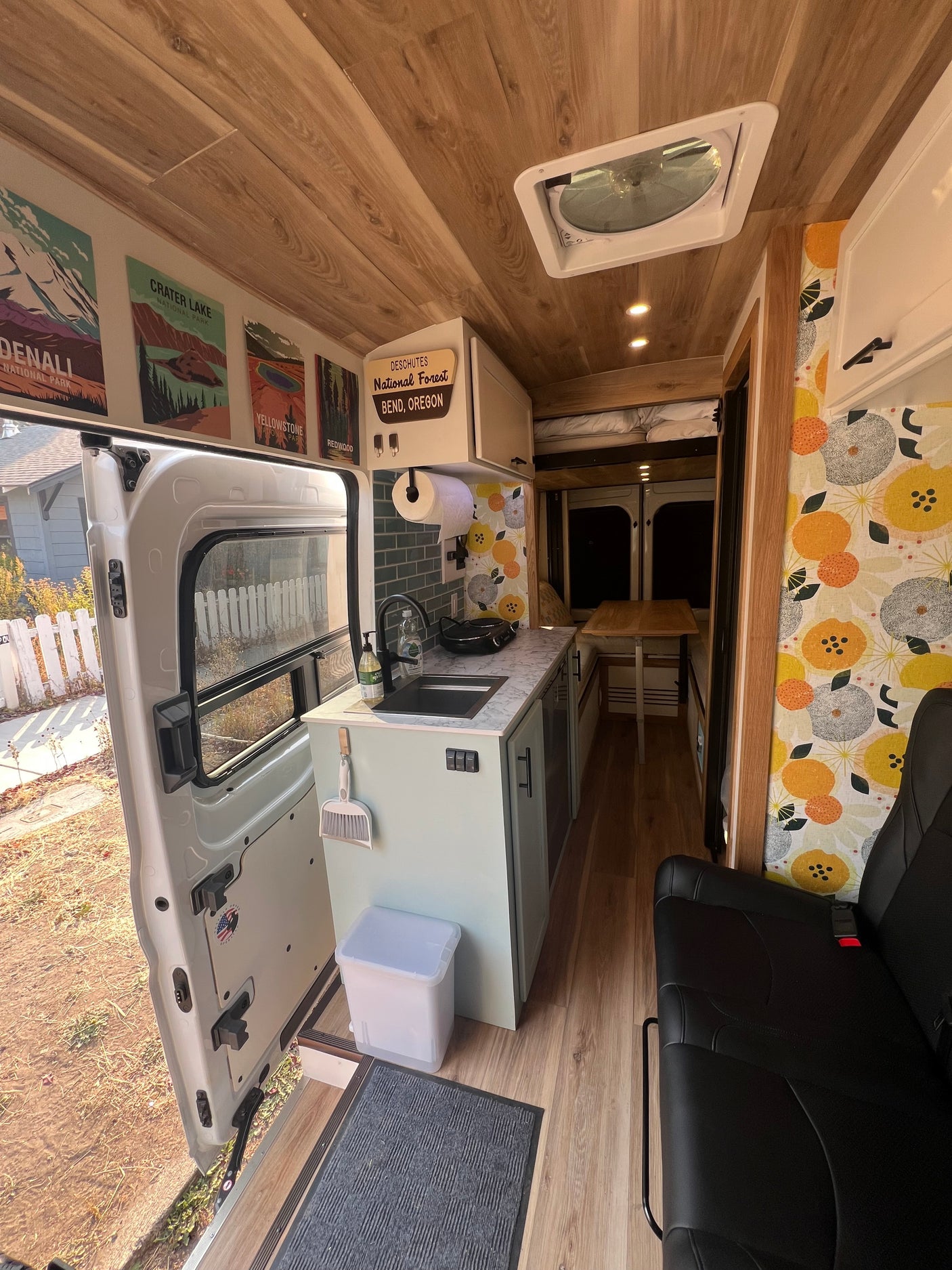 Step into this modern RV rental's camper van interior, featuring a functional kitchen, cozy living space, and wood-paneled ceiling.