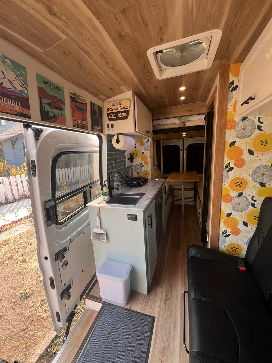 Step into this modern RV rental's camper van interior, featuring a functional kitchen, cozy living space, and wood-paneled ceiling.