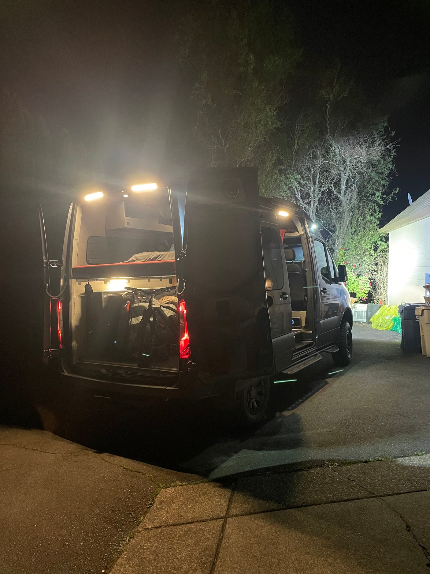 Illuminated RV rental at night with open rear and side doors, revealing a cozy bed and bike inside.
