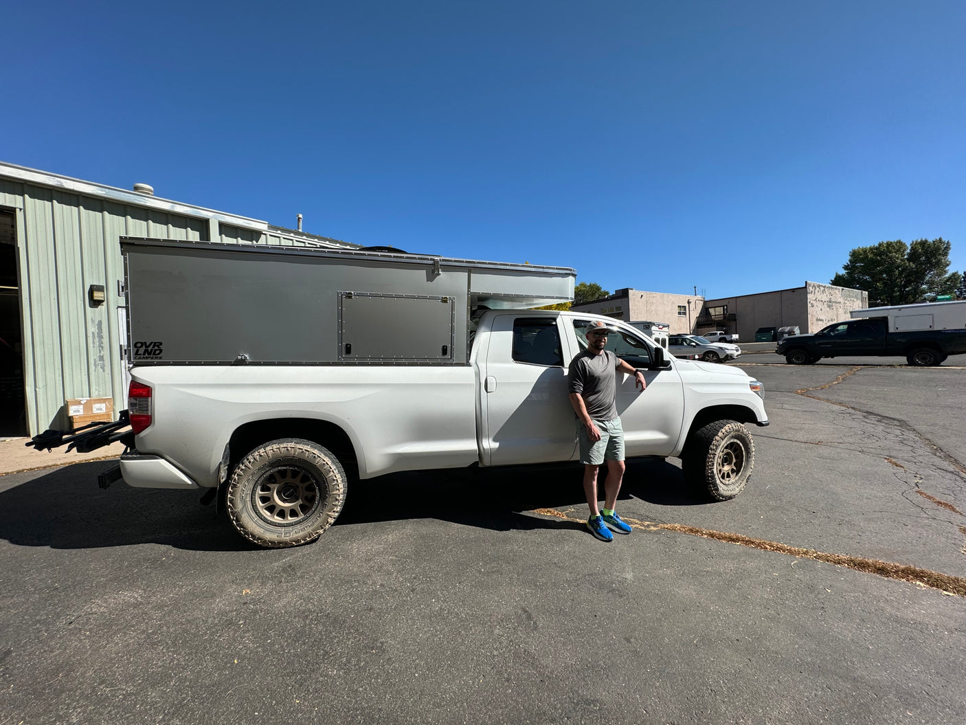 Man with his white OVR LND truck camper, ideal for rugged overland rv rental adventures.