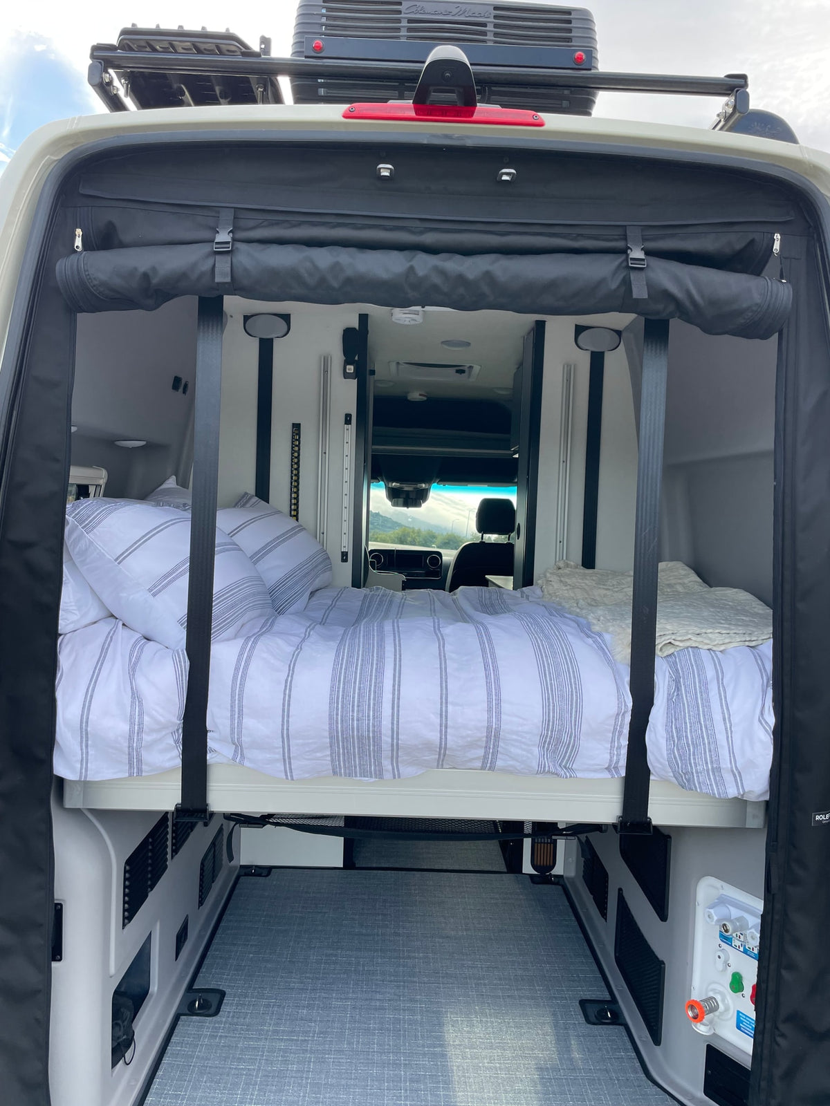 Inside an RV rental camper van: elevated bed with striped bedding, utility connections, and rear storage area, ideal for mobile living. — photo 5