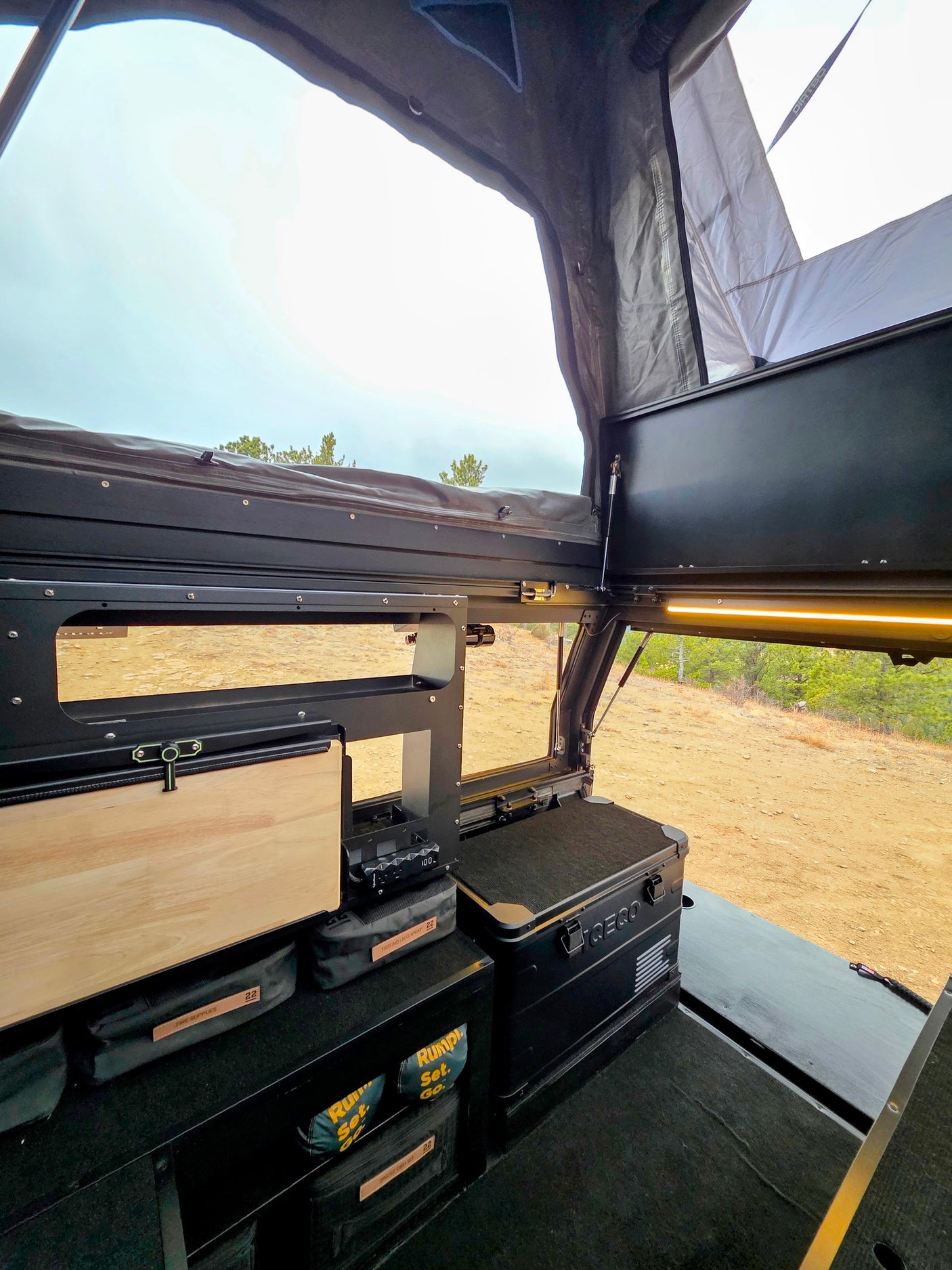 Interior of an overland RV rental camper with modular storage, a fridge, and a pop-top tent, ready for adventure.