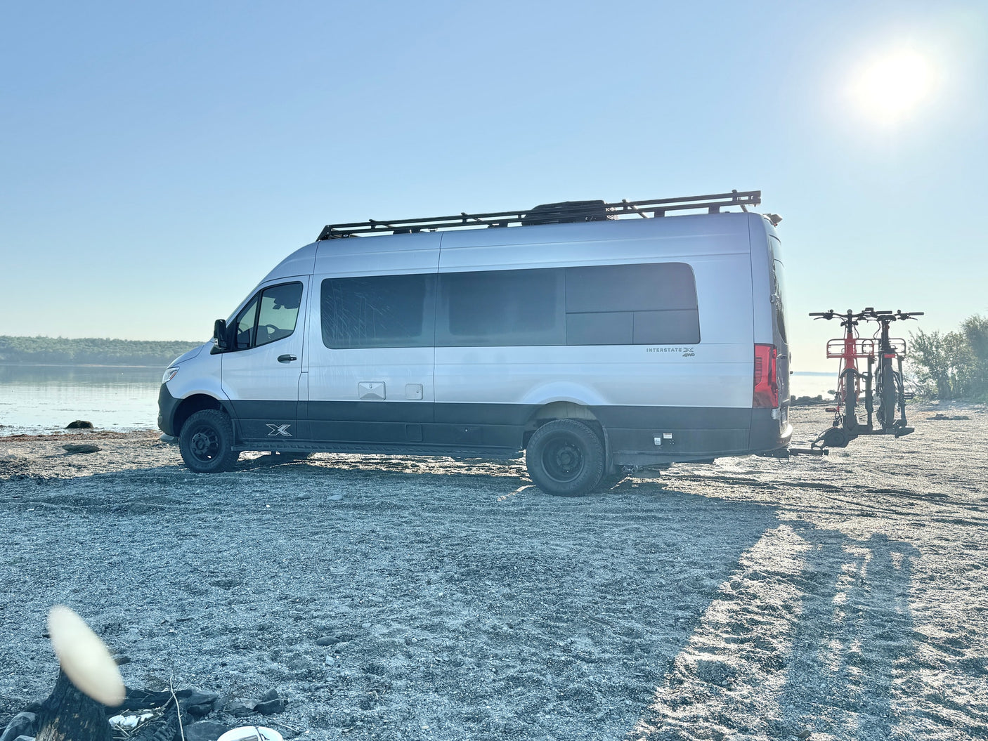 This silver Mercedes-Benz Sprinter rv rental camper van is parked on a gravel shore with bikes