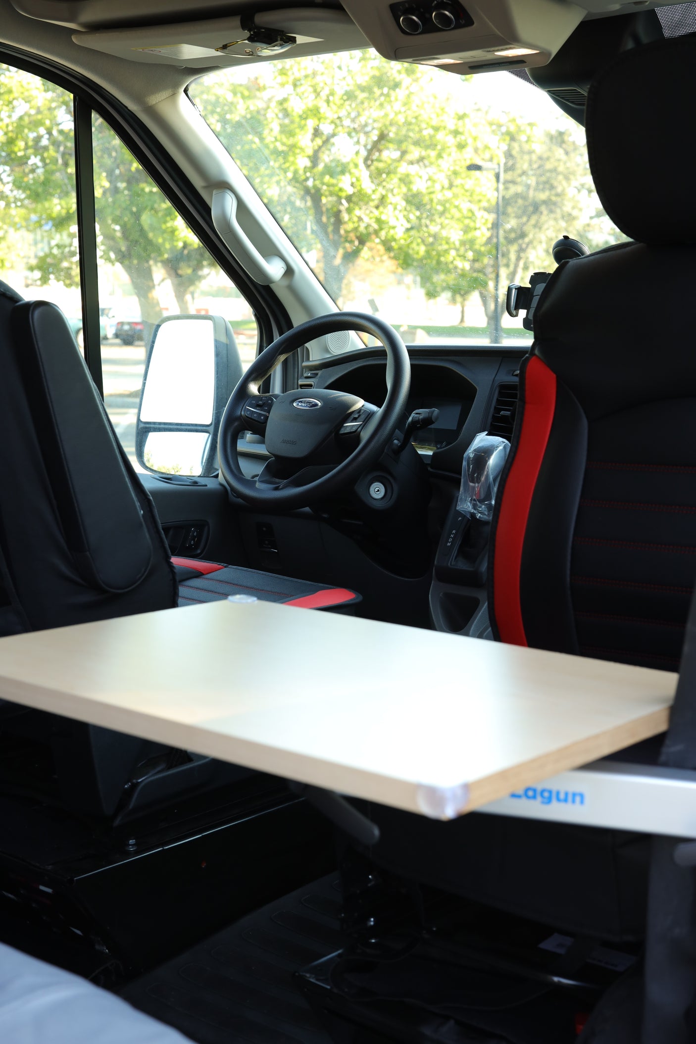 RV rental: Ford Transit interior with black seats, dashboard, and an adjustable Lagun table extending from the side.