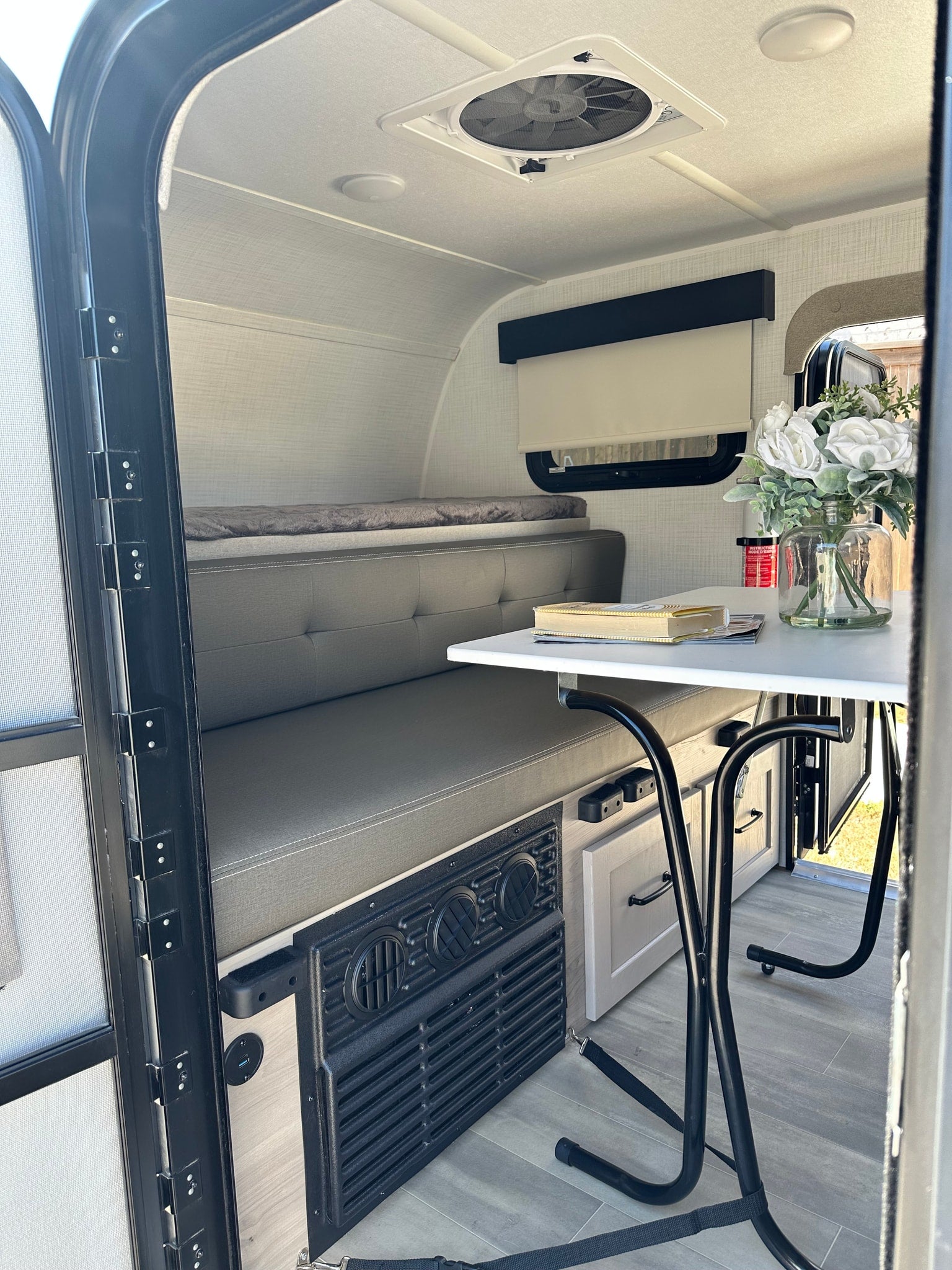 RV rental interior: A compact space with a grey dinette, bed area, table, and ceiling fan for comfortable travel.