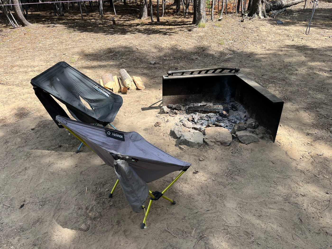 Perfect RV rental campsite: two Helinox chairs, a fire pit with ashes, and firewood in a sunny woodland. — photo 10