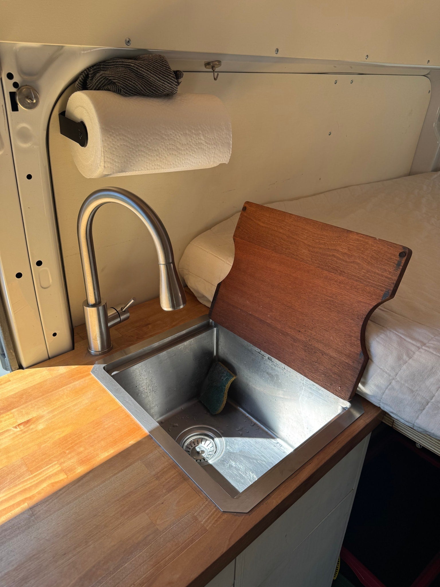 Compact RV rental kitchen with a stainless steel sink, gooseneck faucet, wooden counter, and paper towel holder.