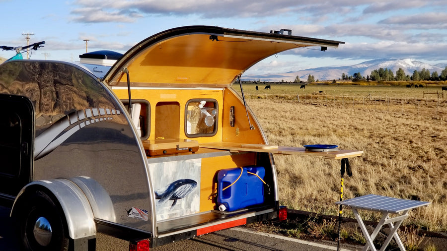 RV rental teardrop camper: outdoor kitchen in stunning field with mountains & cattle. Ready for adventure!