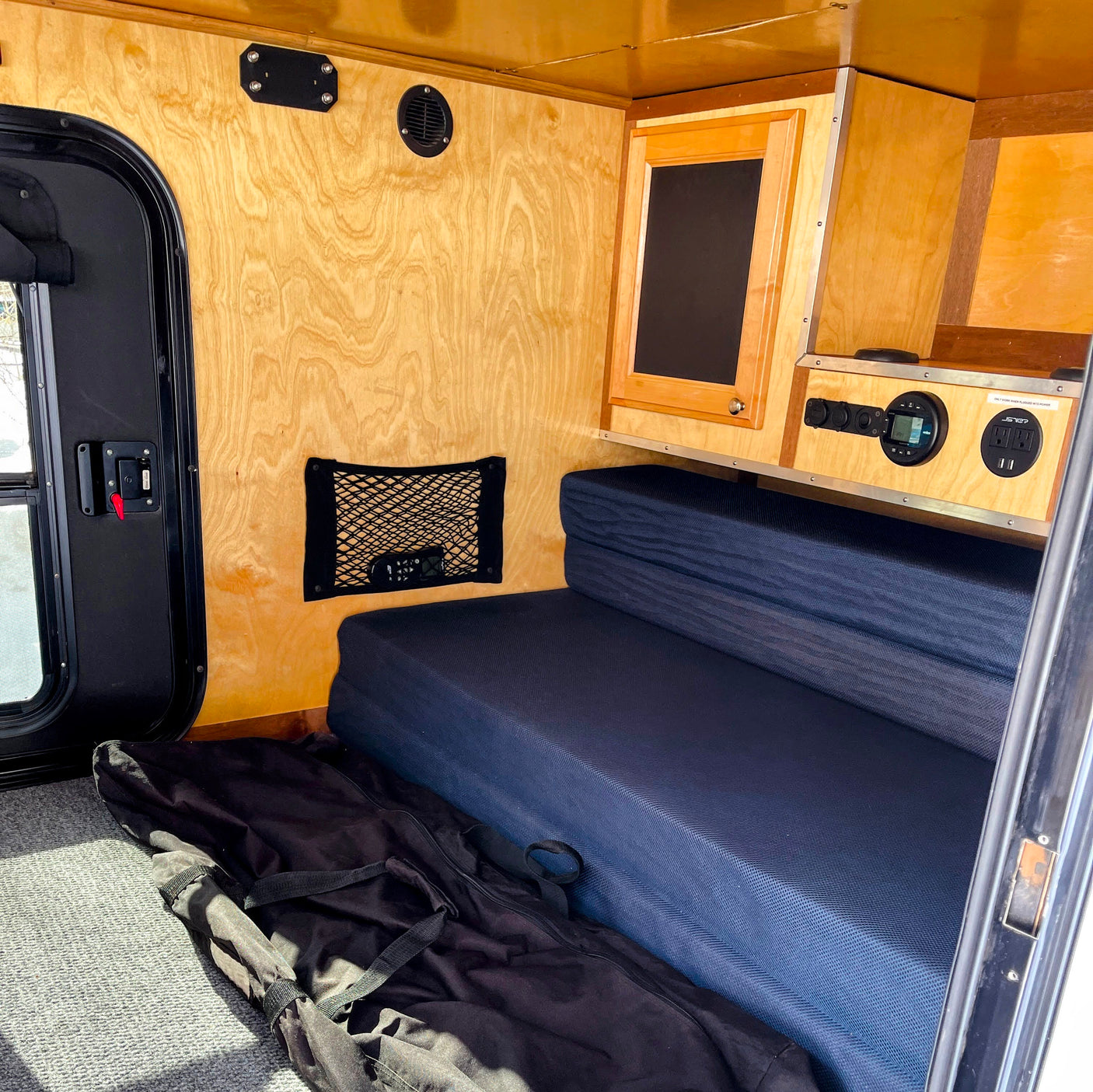Cozy RV rental interior featuring light wood paneling, a dark blue bench/bed, integrated control panel, and a side door.