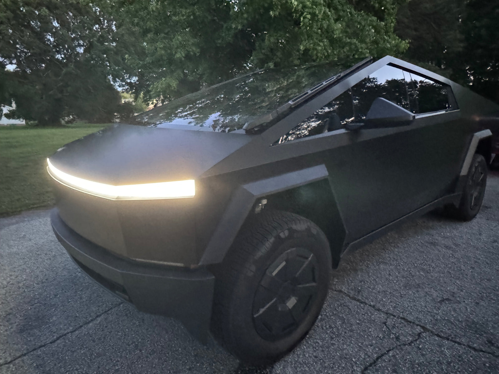 A sleek Tesla Cybertruck, front light on, parked. This electric truck offers unique trips; think beyond traditional RV rental.