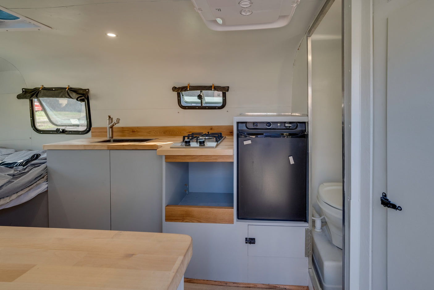 Compact RV rental interior with a bright kitchen featuring a sink, stove, fridge, and a peek into the bathroom.