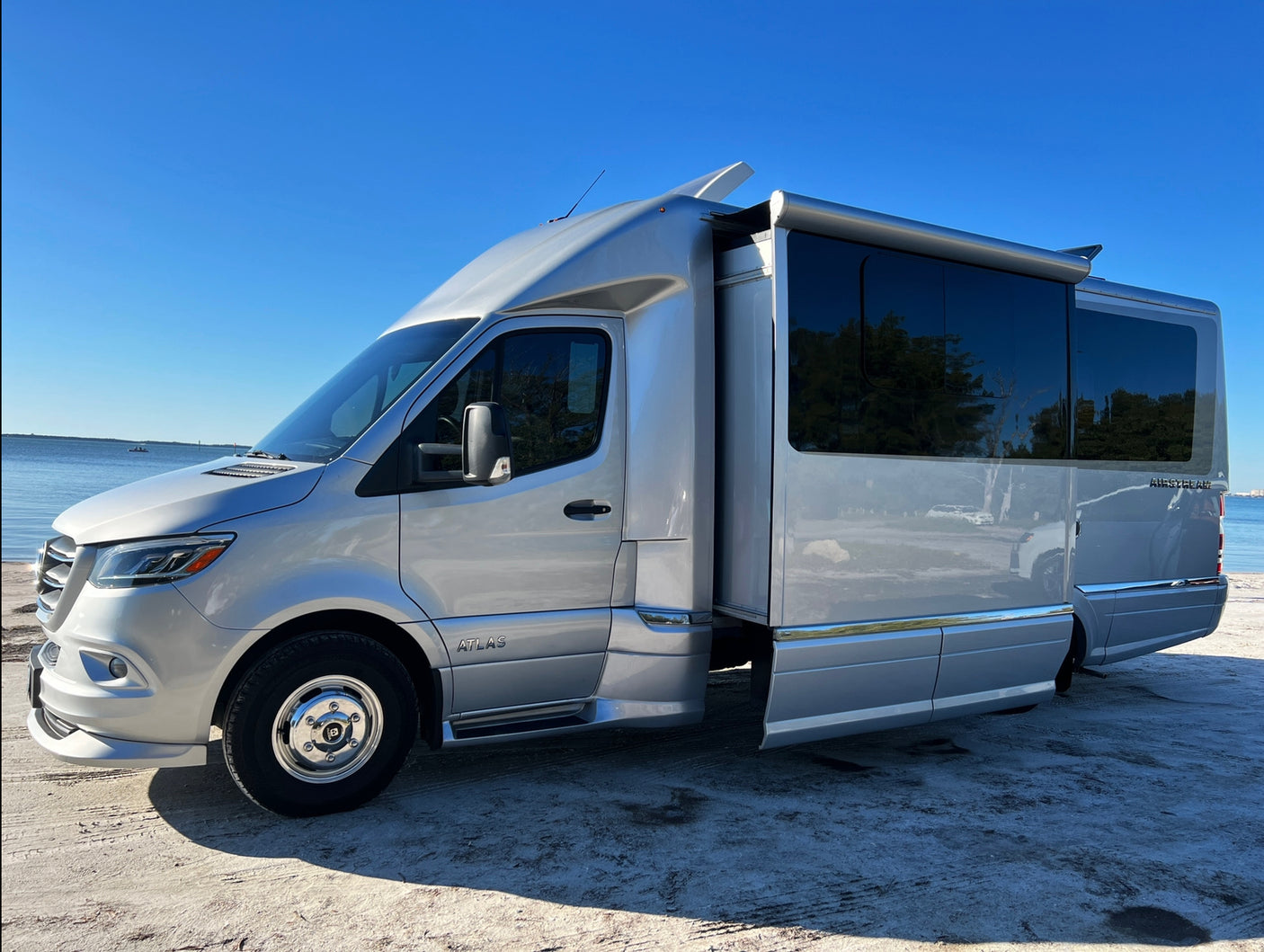 This sleek silver Airstream Atlas RV rental, a Mercedes-Benz Sprinter-based motorhome, enjoys a sunny waterside spot.