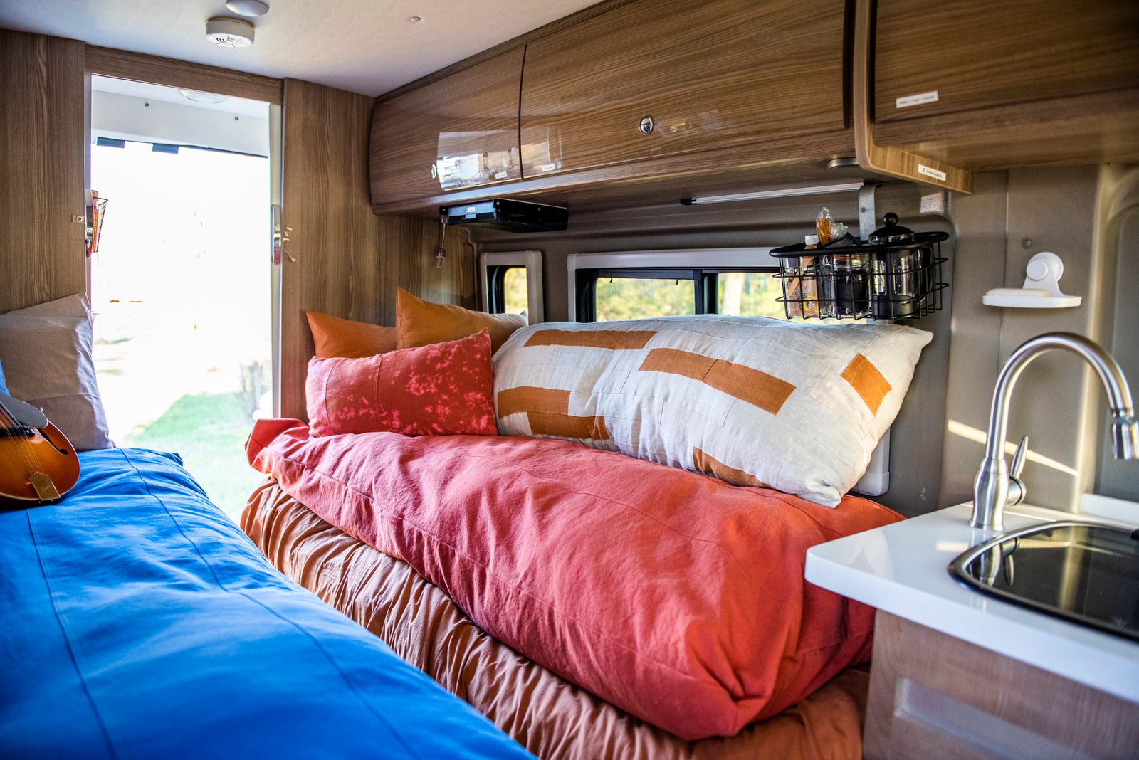 Inside a comfy **rv rental**: bed with colorful pillows, kitchen area, and a mandolin for road trip tunes.
