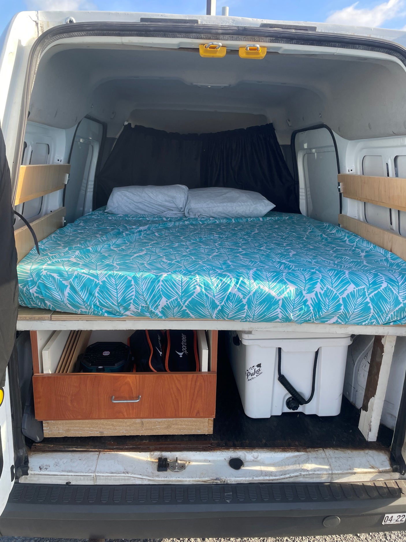 Cozy RV rental camper van interior with a bed, tropical sheets, pillows, and under-bed storage including a cooler.