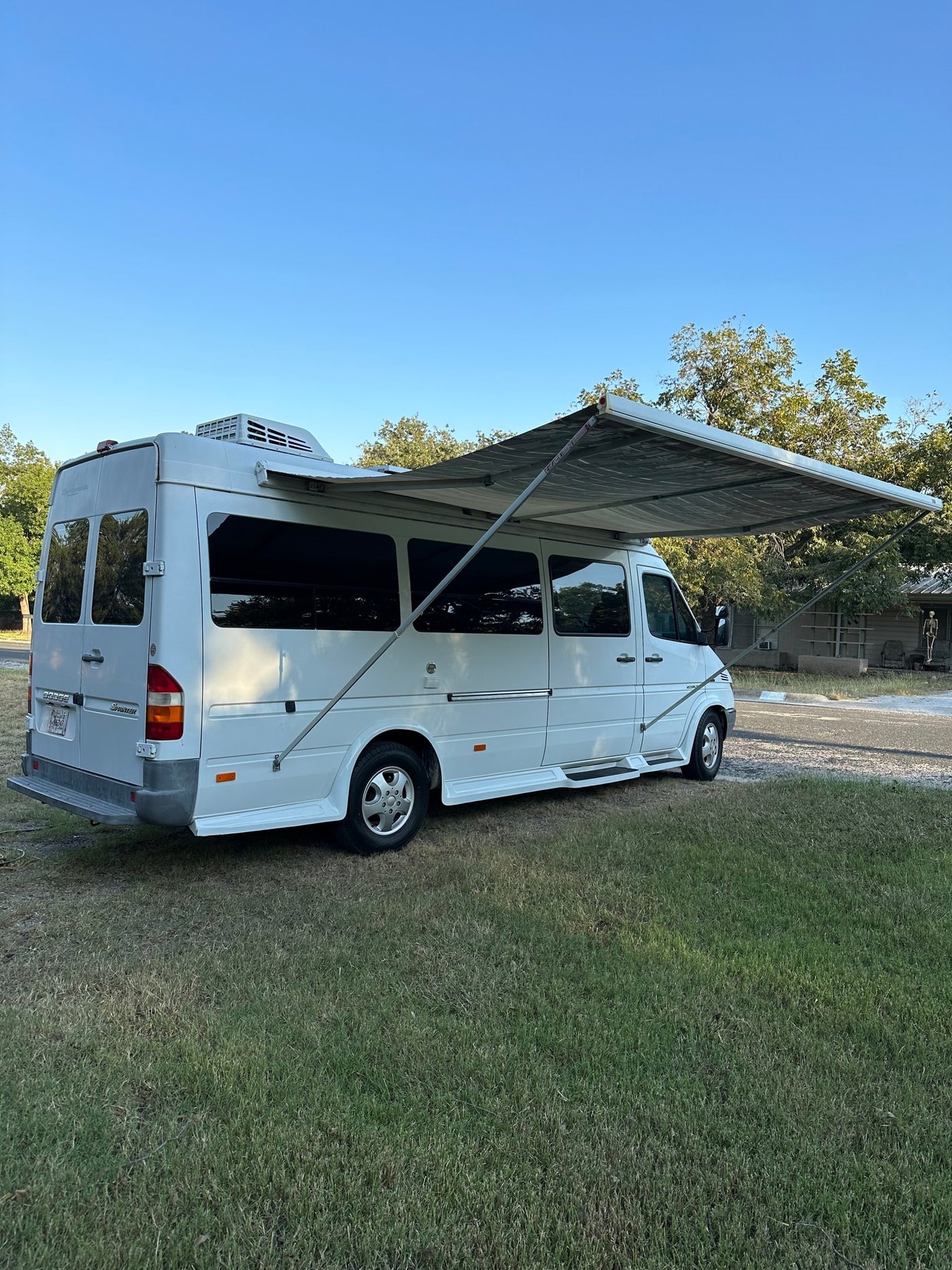 White Dodge Sprinter camper van with extended awning on grass — photo 1
