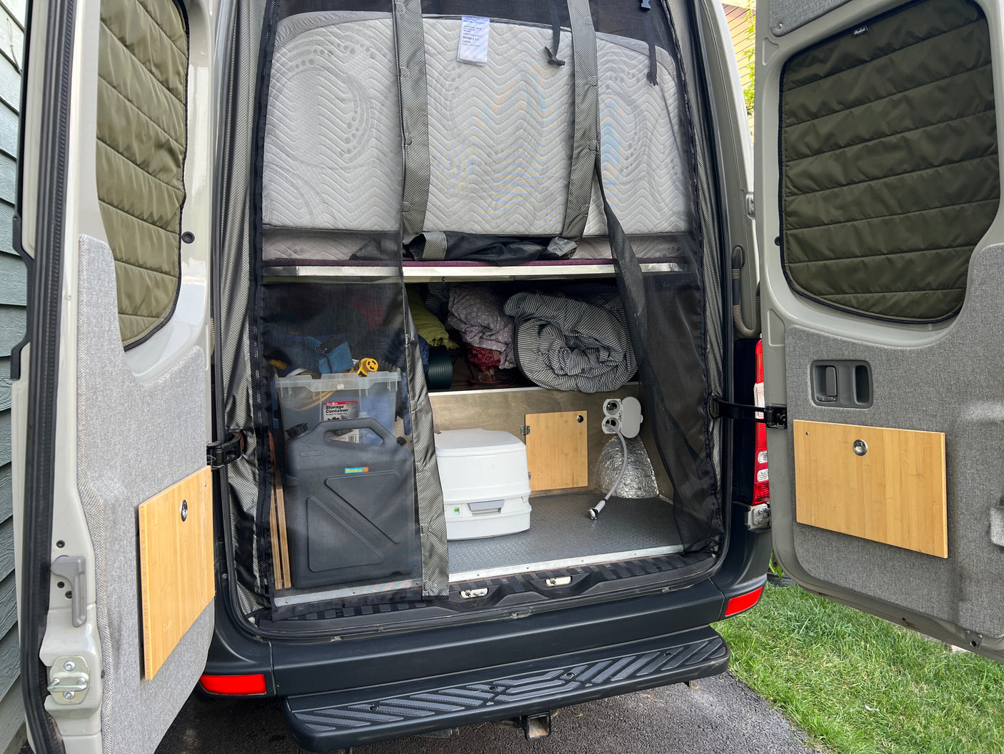 RV rental ready for adventure! Rear van view shows organized storage, bed, portable toilet & outdoor shower.