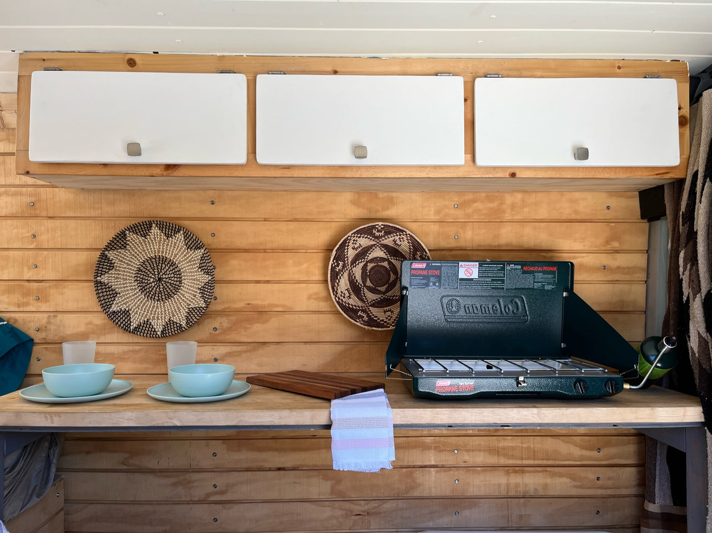 Inside an RV rental: a compact kitchen with wood paneling, white overhead cabinets, a Coleman propane stove, and dining essentials. — photo 5