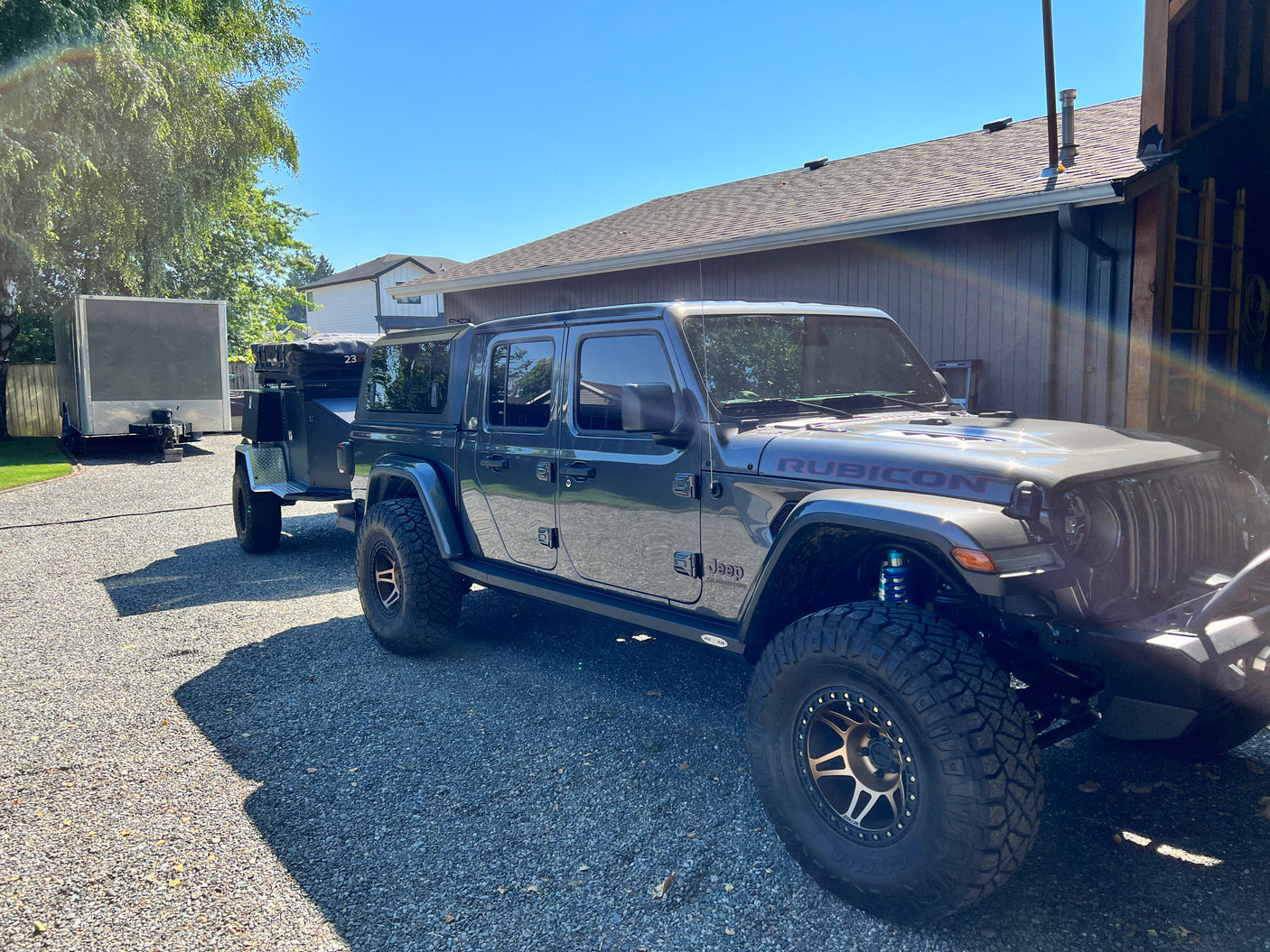 Modified grey Jeep Gladiator towing an off-road camping trailer, with another trailer nearby. Ideal setup for an RV rental adventure!