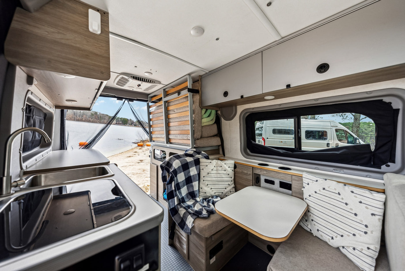parked in a lot.|Cozy RV rental camper van interior: a comfortable bed with quilted pillows & scenic views through the mesh screen.|Cozy RV rental interior with kitchen