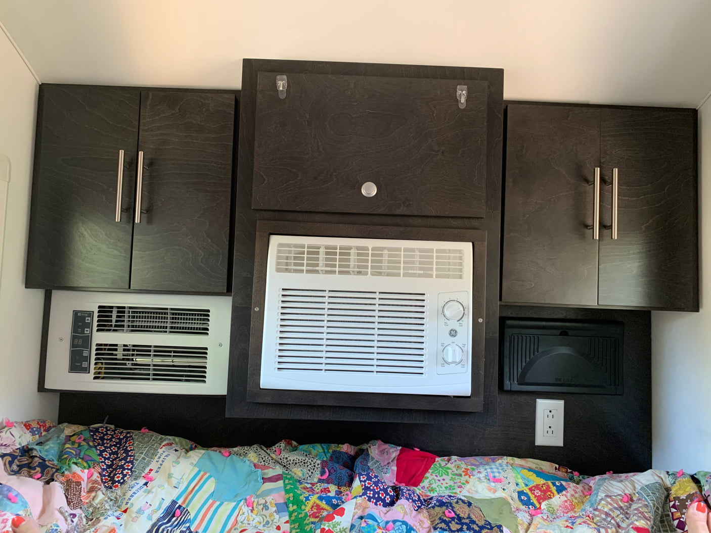 RV rental bedroom with dark custom cabinets, two built-in AC units, power outlet, and a vibrant patchwork quilt.