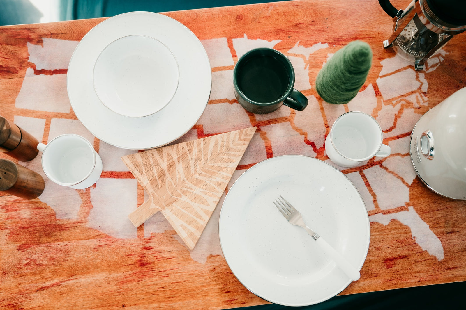 RV rental kitchen setup: Plates, mugs, kettle & French press on a table with a unique map-like pattern.