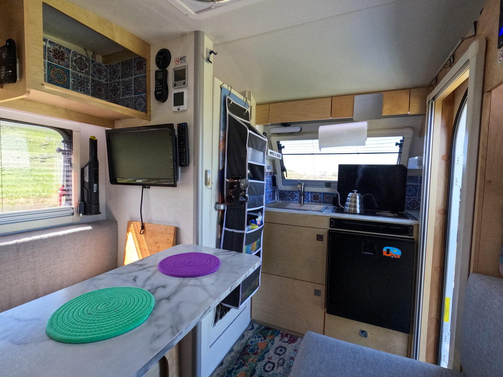 Cozy rv rental interior featuring a compact kitchen, dining table with colorful placemats, TV, and smart storage.