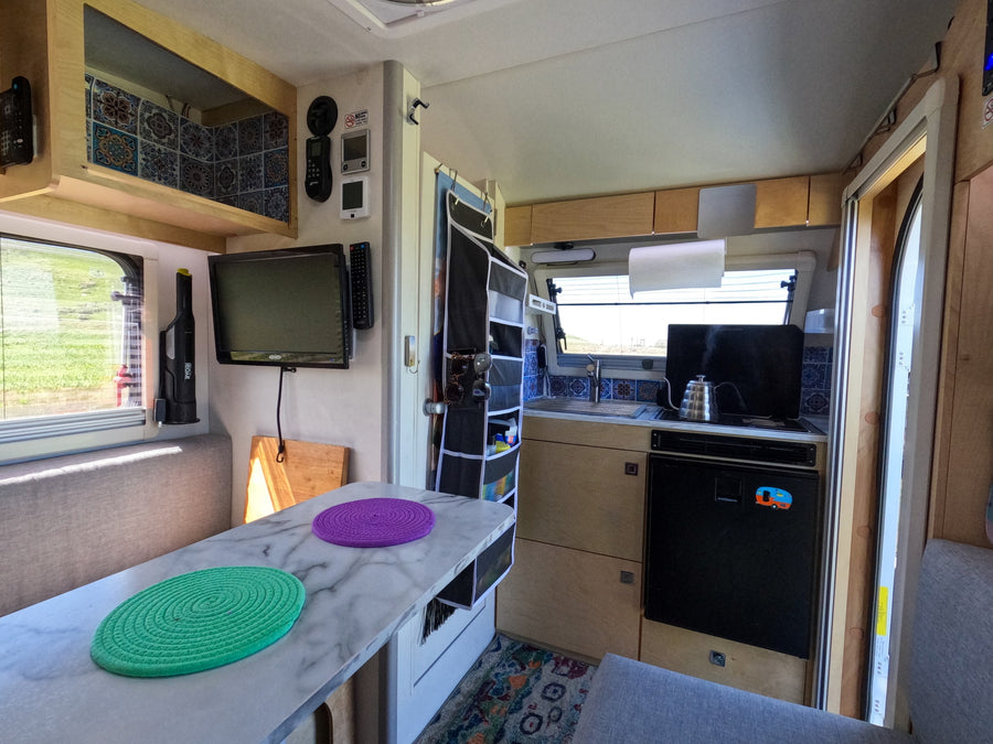 Cozy rv rental interior featuring a compact kitchen, dining table with colorful placemats, TV, and smart storage.