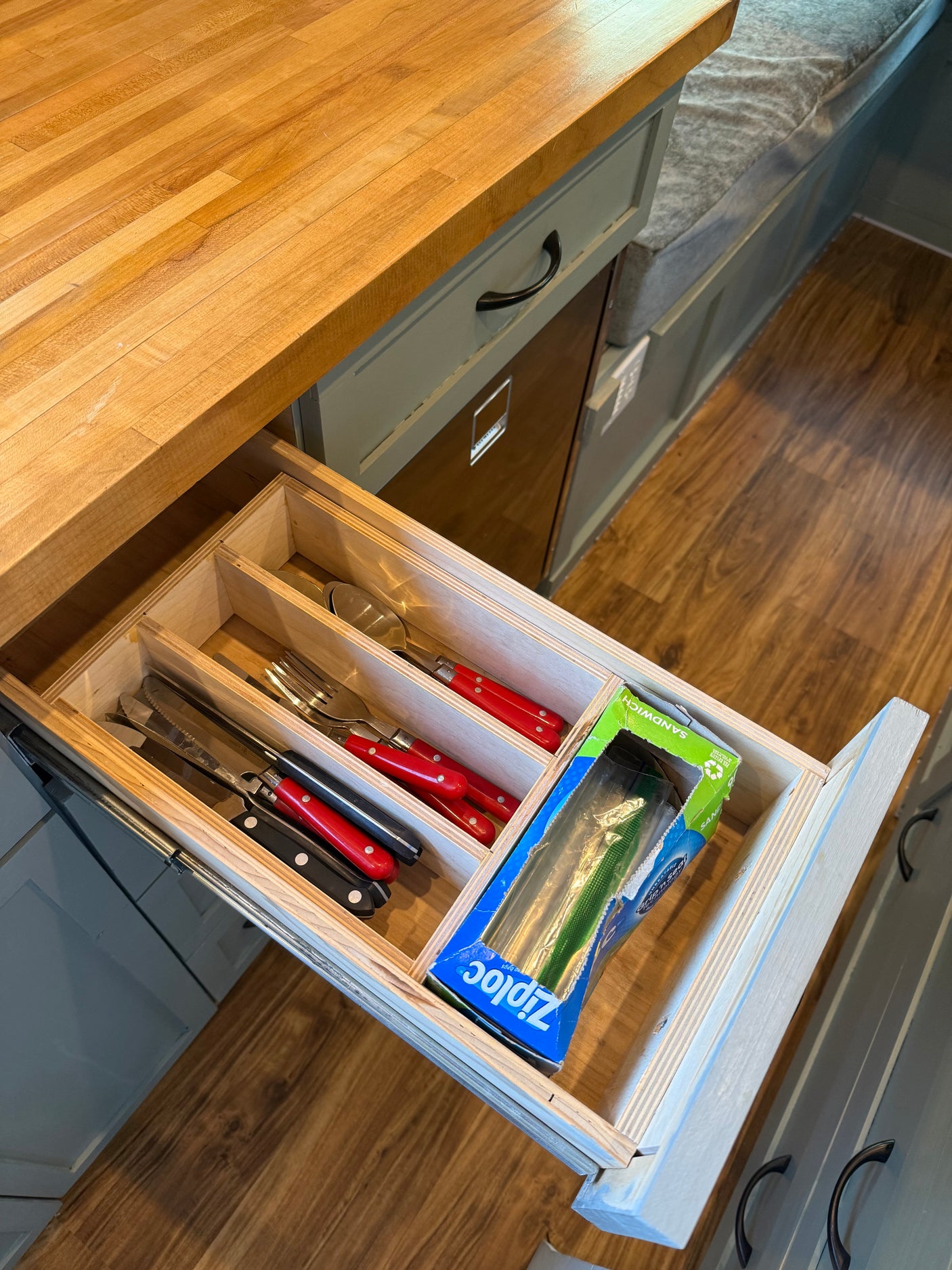 RV rental kitchen drawer open, showing organized cutlery with red handles, Ziploc bags, and a wooden countertop.
