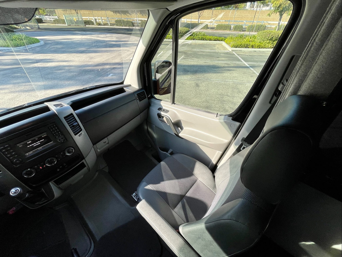 Inside a bright RV rental's front cabin, showing the dashboard, driver & passenger seats, and clear exterior view.