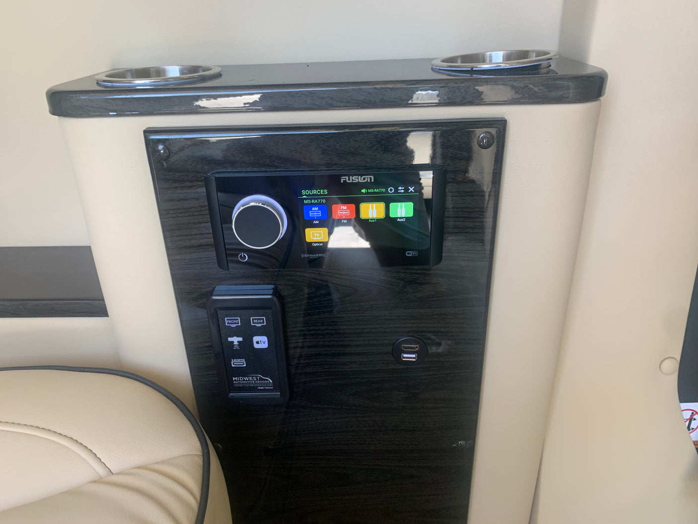 Close-up of a luxury RV rental's custom entertainment panel, featuring a Fusion stereo, Apple TV, HDMI, and USB.