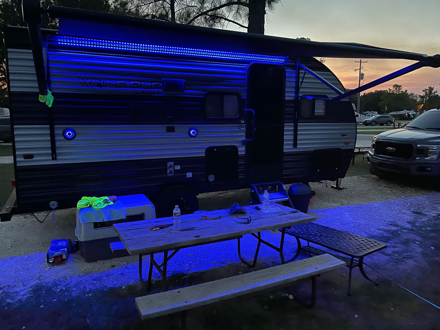 perfect for a stargazing camping adventure.|Enjoying the night at an RV rental site! Blue LED lights highlight the camper and picnic area at dusk.|An RV rental travel trailer is set up at a sunny campsite with a truck