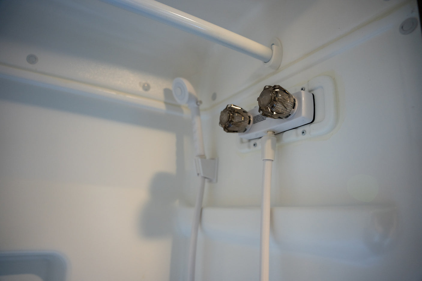 RV rental shower: a compact white shower stall with handheld showerhead and dual control knobs.