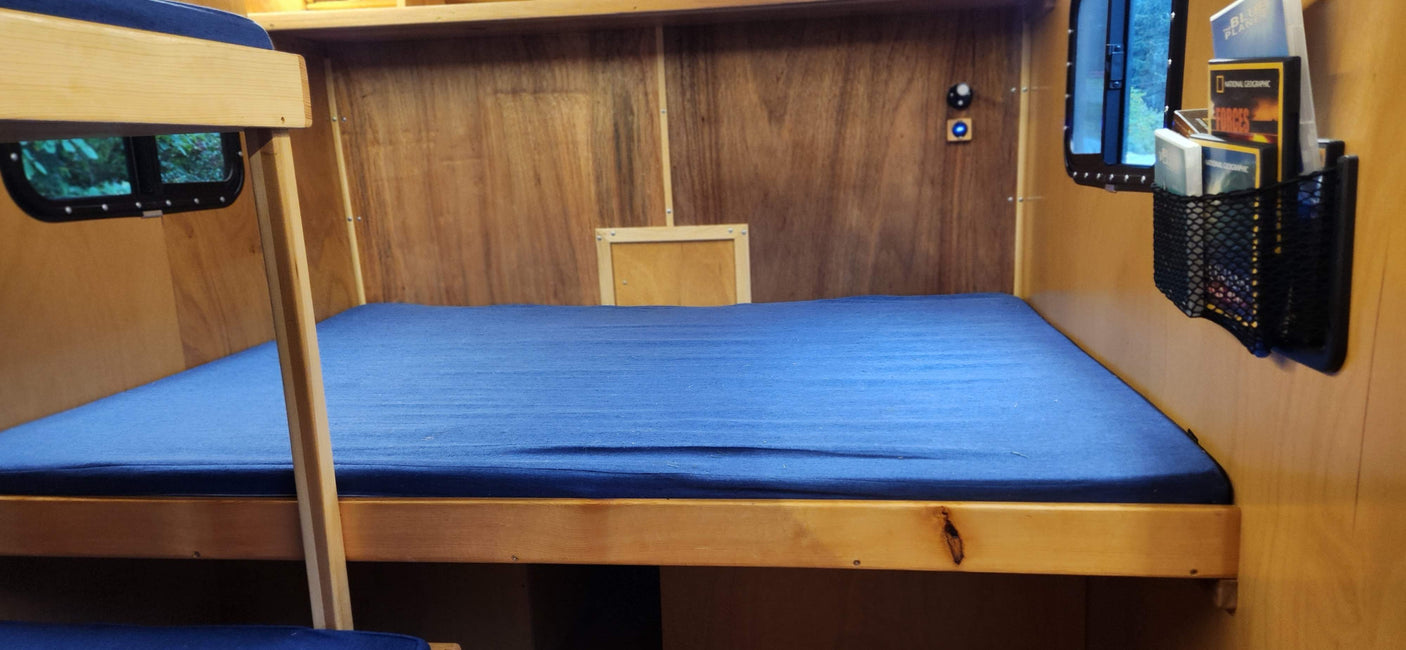 rv rental: A cozy, wood-paneled interior featuring blue bunk beds, a small window, and a wall-mounted magazine holder.