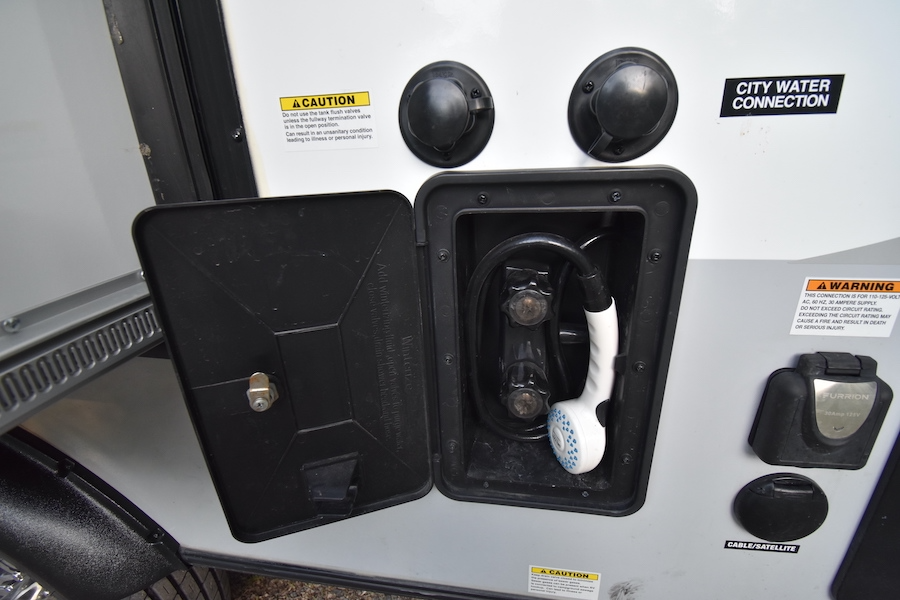 RV rental external utility connections: an open outdoor shower, city water, electrical, and cable/satellite hookups.