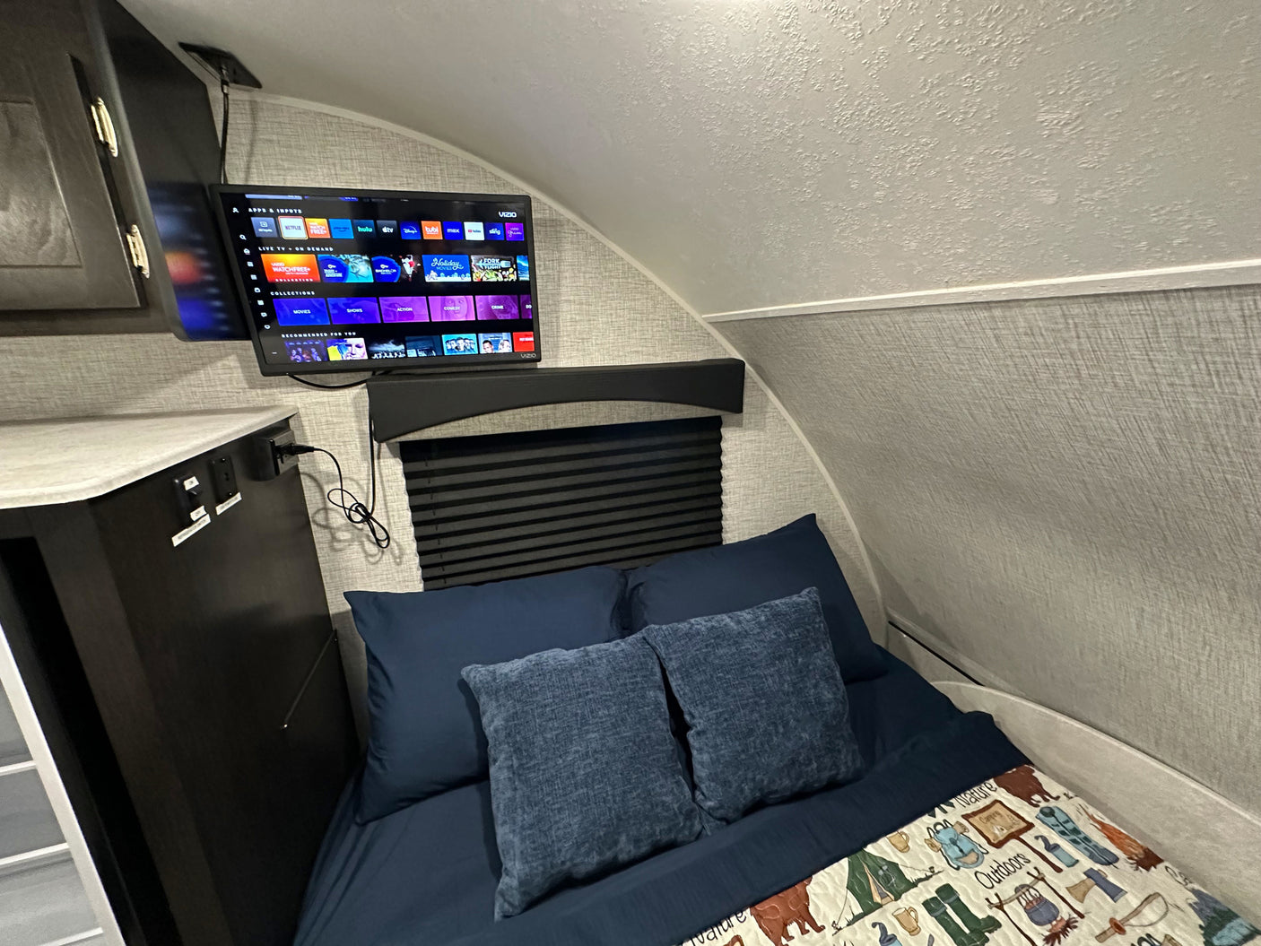 Cozy RV rental bedroom with a mounted TV showing streaming options, a comfortable bed, and a nature-themed blanket.