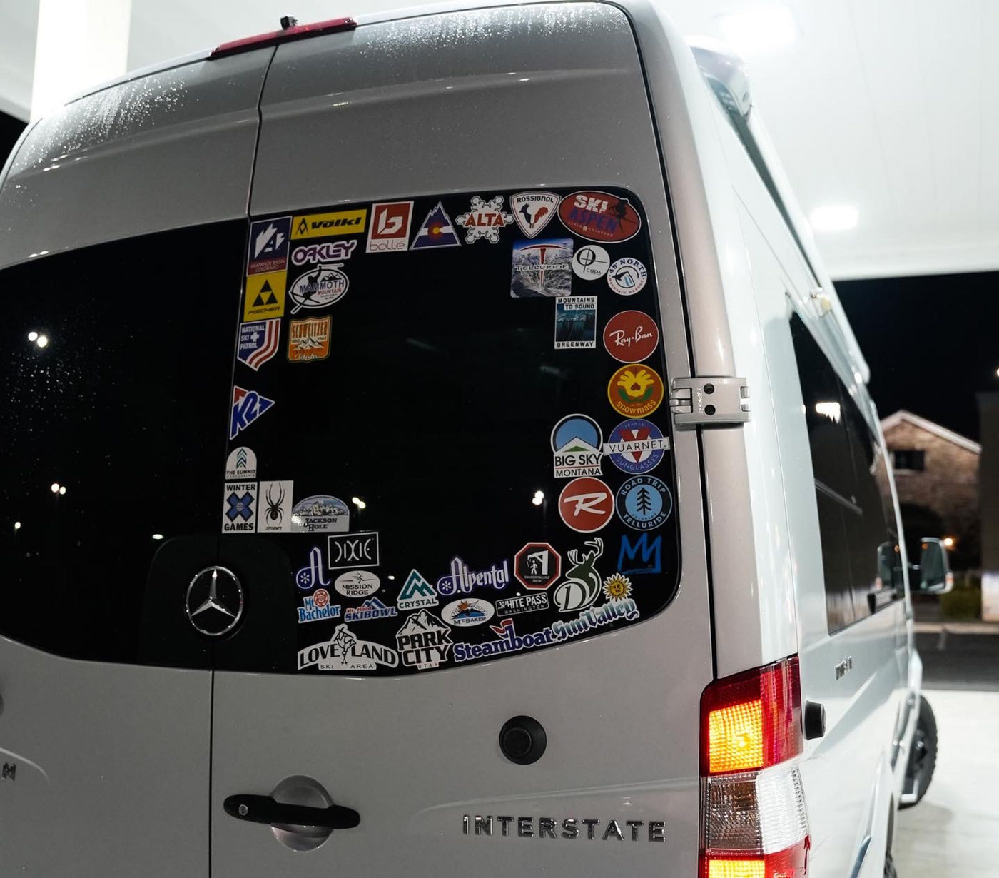 An Airstream Interstate rv rental's rear window, covered in ski resort and outdoor brand stickers from various adventures. — photo 13